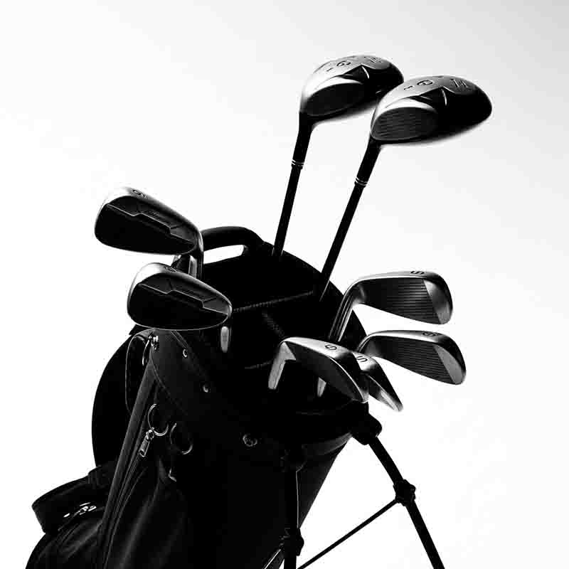 Ein Golfball liegt auf einem Tisch neben einem Holz-Tee und einem Golfhandschuh. Ein Golfschläger liegt dahinter und wirft einen Schatten.